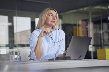 Geschäftsfrau mit Brille und Laptop am Schreibtisch im Büro - RBF08795