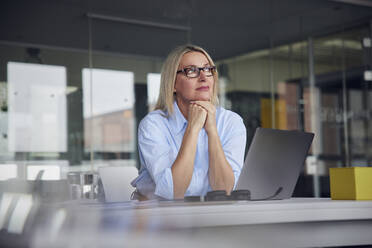 Businesswoman wearing eyeglasses with laptop at desk in office - RBF08796