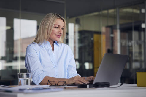Lächelnde Geschäftsfrau mit Laptop am Schreibtisch im Büro - RBF08799