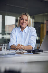 Glückliche Geschäftsfrau mit Laptop am Schreibtisch im Büro - RBF08804