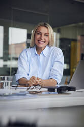 Happy businesswoman with laptop at desk in office - RBF08804