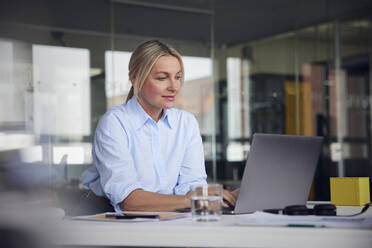 Lächelnde Geschäftsfrau mit Laptop am Schreibtisch im Büro - RBF08806