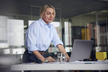 Lächelnde Geschäftsfrau arbeitet am Laptop am Schreibtisch im Büro - RBF08810