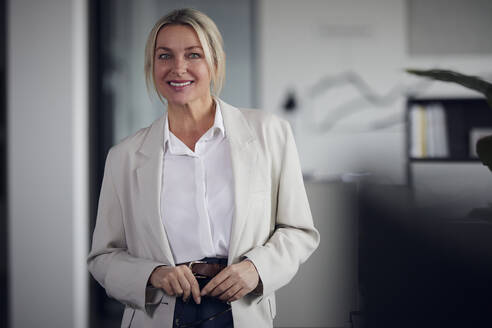 Lächelnde Geschäftsfrau mit blondem Haar im Büro stehend - RBF08820