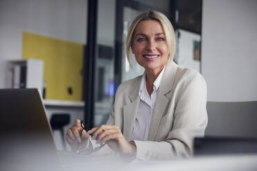 Glückliche Geschäftsfrau mit Laptop am Schreibtisch im Büro - RBF08826