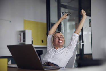 Happy businesswoman stretching with arms raised in office - RBF08834