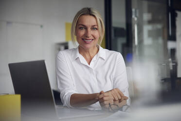 Lächelnde Geschäftsfrau mit Laptop am Schreibtisch im Büro - RBF08837