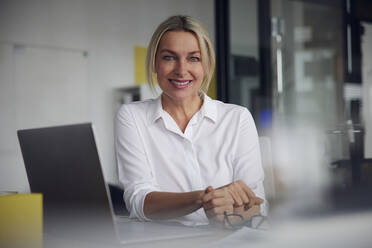 Smiling businesswoman with laptop at desk in office - RBF08837