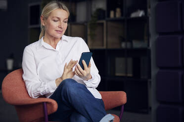 Businesswoman using mobile phone sitting on chair in office - RBF08845