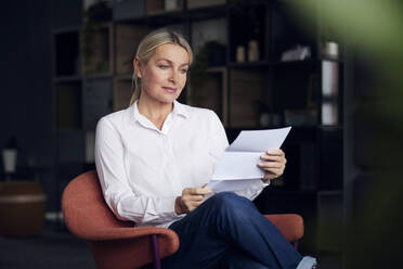 Businesswoman analyzing document sitting on chair in office - RBF08855