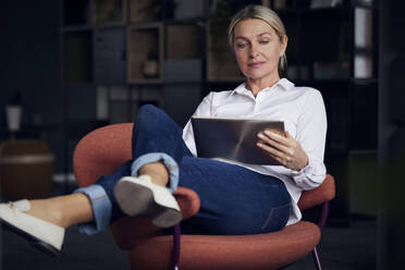 Businesswoman using tablet PC sitting on chair in office - RBF08856