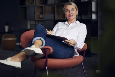 Lächelnde Geschäftsfrau mit Tablet-PC auf einem Stuhl im Büro sitzend - RBF08857