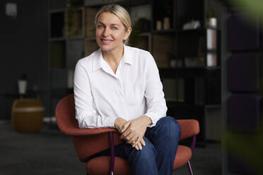 Happy businesswoman with hands clasped sitting on chair - RBF08860