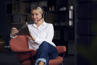 Businesswoman with headset using tablet PC sitting on chair - RBF08861