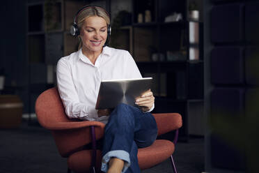 Lächelnde Geschäftsfrau mit Headset und Tablet-PC auf einem Stuhl sitzend - RBF08862