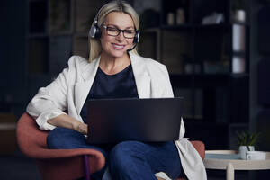 Lächelnde Geschäftsfrau mit Headset bei der Arbeit am Laptop im Büro - RBF08871