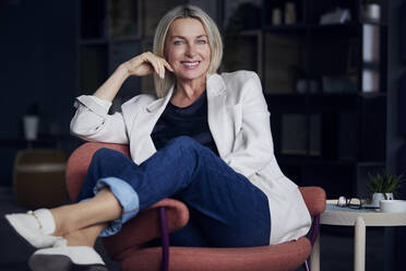 Smiling businesswoman sitting on chair at home office - RBF08875