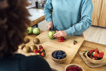 Woman cutting apple standing at table in kitchen - GIOF15094