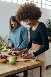 Frauen schneiden Erdbeeren und Äpfel am Tisch in der Küche zu Hause - GIOF15098