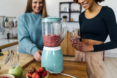 Happy woman preparing smoothie in kitchen at home - GIOF15115