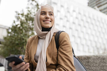 Smiling young businesswoman with mobile phone at office park - JCCMF05881