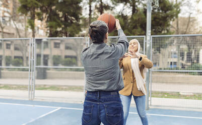Businesswoman playing basketball with young colleague at sports court - JCCMF05897