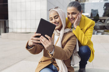 Smiling young businesswoman taking selfie with colleague through tablet PC at office park - JCCMF05911