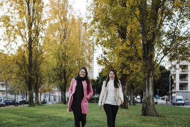 Glückliche Schwestern, die in einem öffentlichen Park vor Bäumen spazieren gehen - DCRF01091