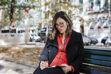 Frau schreibt in Buch auf Bank sitzend - DCRF01108