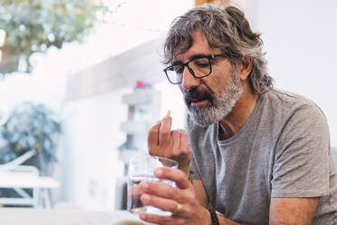 Älterer Mann nimmt Medizin mit einem Glas Wasser ein - PNAF03470