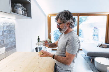 Mann mit Glasgefäß an der Küchentheke stehend - PNAF03485