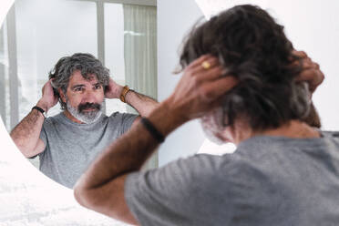 Älterer Mann mit Kopf im Haar schaut in den Spiegel - PNAF03510