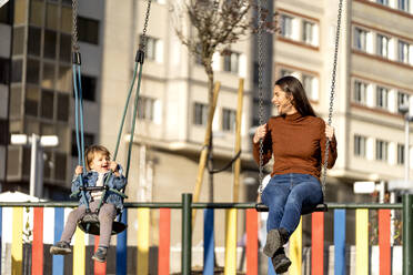 Happy young woman and son on swing in park - OCMF02373