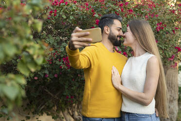 Heterosexuelles Paar reibt sich die Nasen und macht ein Selfie mit dem Smartphone im Garten - SVKF00072
