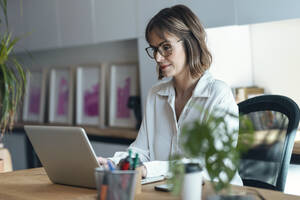 Geschäftsfrau mit Laptop am Schreibtisch im Büro - JSRF01974