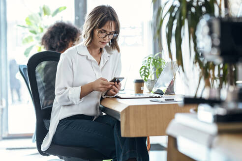 Geschäftsfrau mit Smartphone am Schreibtisch sitzend im Büro - JSRF01977