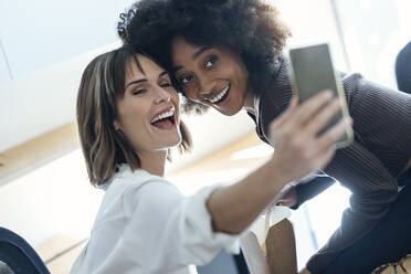 Happy businesswoman taking selfie with colleague through mobile phone in office - JSRF01992