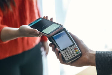 Hand einer Frau beim kontaktlosen Bezahlen mit dem Mobiltelefon - JSRF01997