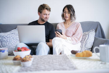 Frau diskutiert über Smartphone mit Mann, der zu Hause auf dem Sofa sitzt - FBAF01890