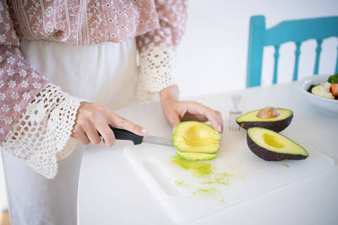 Junge Frau hackt Avocado am Tisch stehend - FBAF01922
