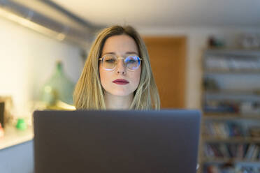 Junge Frau mit Brille arbeitet am Laptop am Tisch - FBAF01958