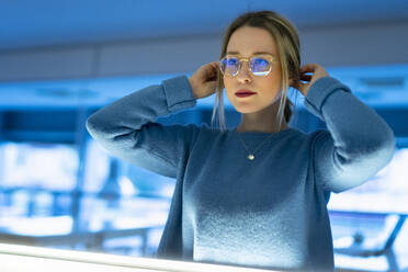 Young woman with hands in hair wearing eyeglasses - FBAF01967