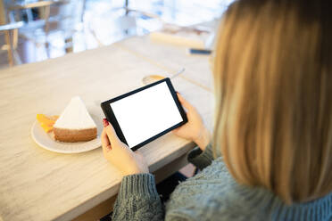 Junge Frau mit blondem Haar, die am Tisch sitzend einen Tablet-PC benutzt - FBAF01976