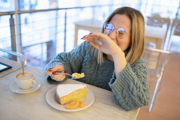 Glückliche junge Frau genießt Zitronenkuchen am Tisch - FBAF01977