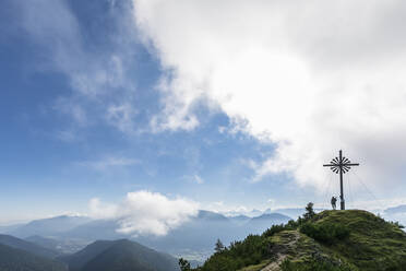Frau steht am Brunstlkopf-Gipfelkreuz auf dem Berg unter bewölktem Himmel - FOF13079