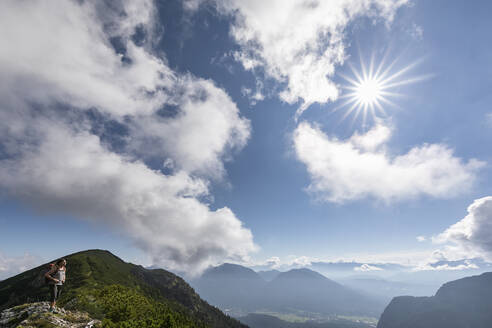 Frau steht auf einem Berg unter bewölktem Himmel an einem sonnigen Tag - FOF13081