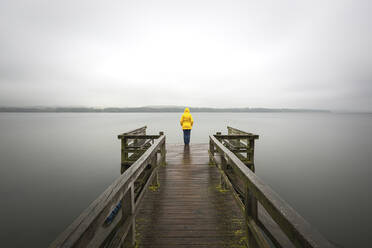 Germany, Schleswig-Holstein, Woman in yellow jacket standing on edge of lakeshore jetty - ASCF01678