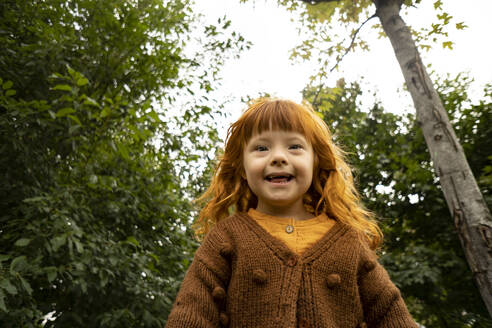 Smiling girl with down syndrome standing in front of trees at public park - SSGF00530