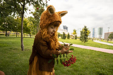 Girl holding berry fruit twig in public park - SSGF00535