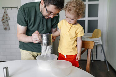 Mann mit Tochter siebt Mehl am Tisch in der Küche - OGF01138